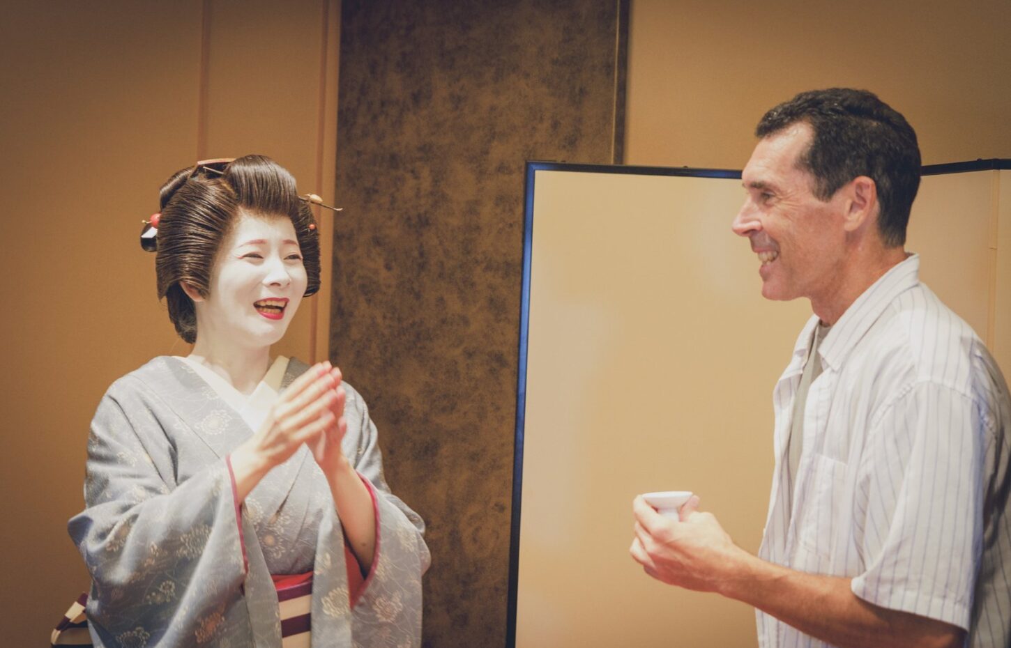 An Asakusa geisha sharing a laugh with a guest at a private tatami banquet room