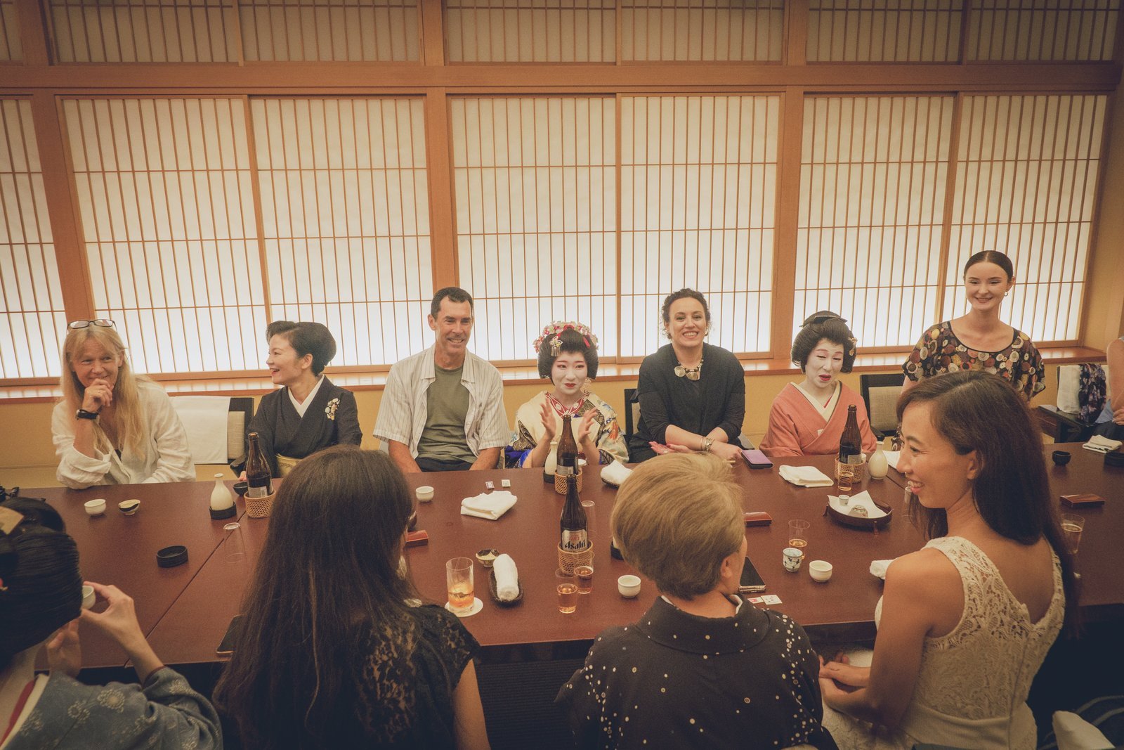 A lively private banquet room in Asakusa with several guests and geisha, the kind of returning gohiiki gathering that supports geisha today