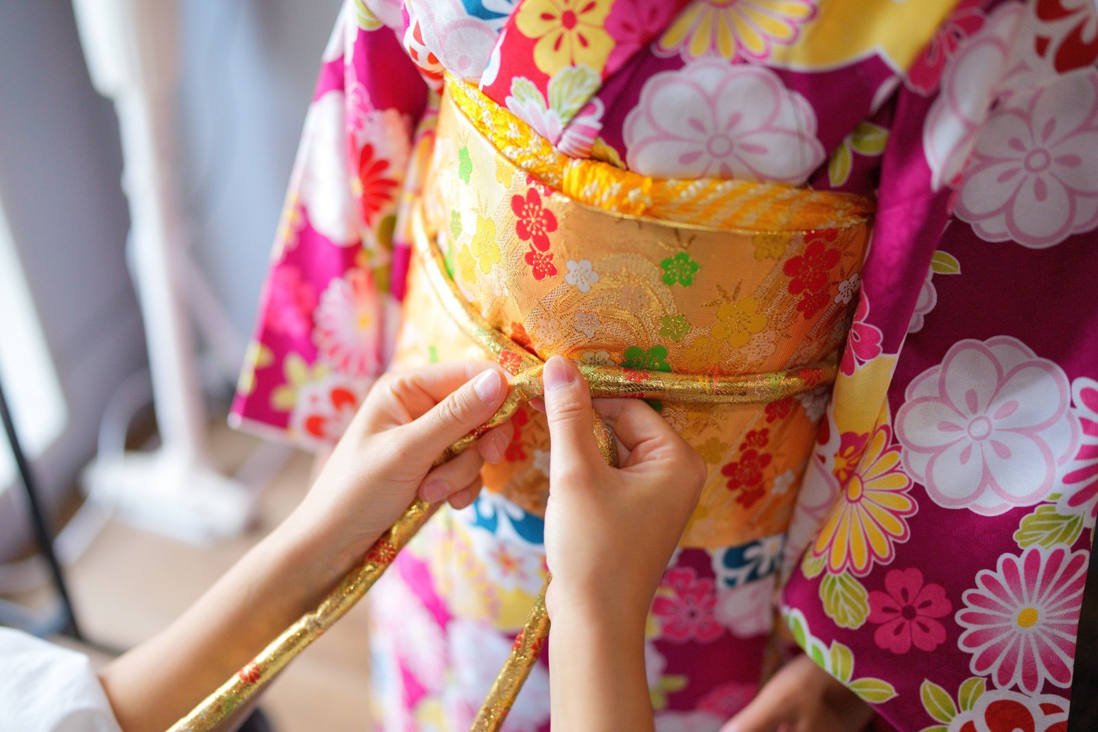 Hands tying the obi cord during kimono dressing, one of the costs a geisha covers herself