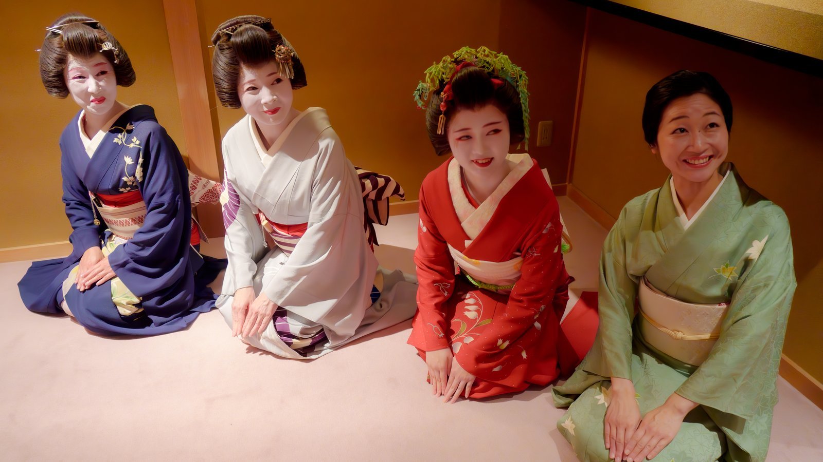 Four Asakusa geisha seated side by side: three tachikata, one of them a hangyoku with the momoware, and a jikata on the right