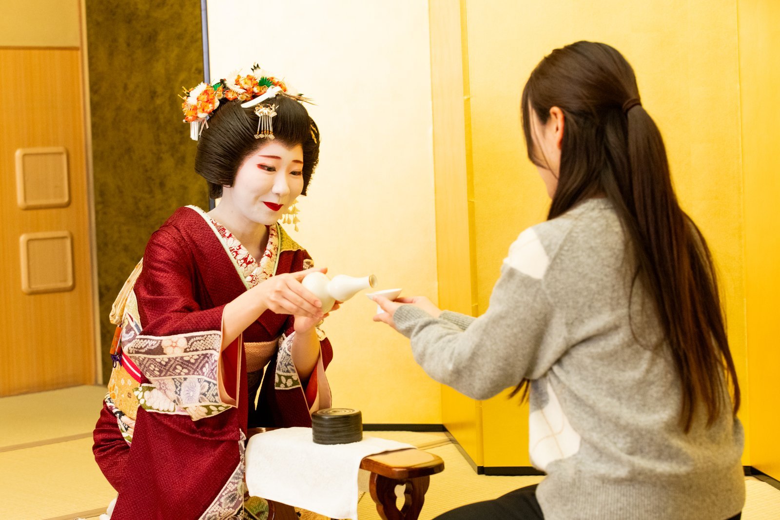 A young Asakusa geisha pouring a drink for a guest at a tatami banquet room