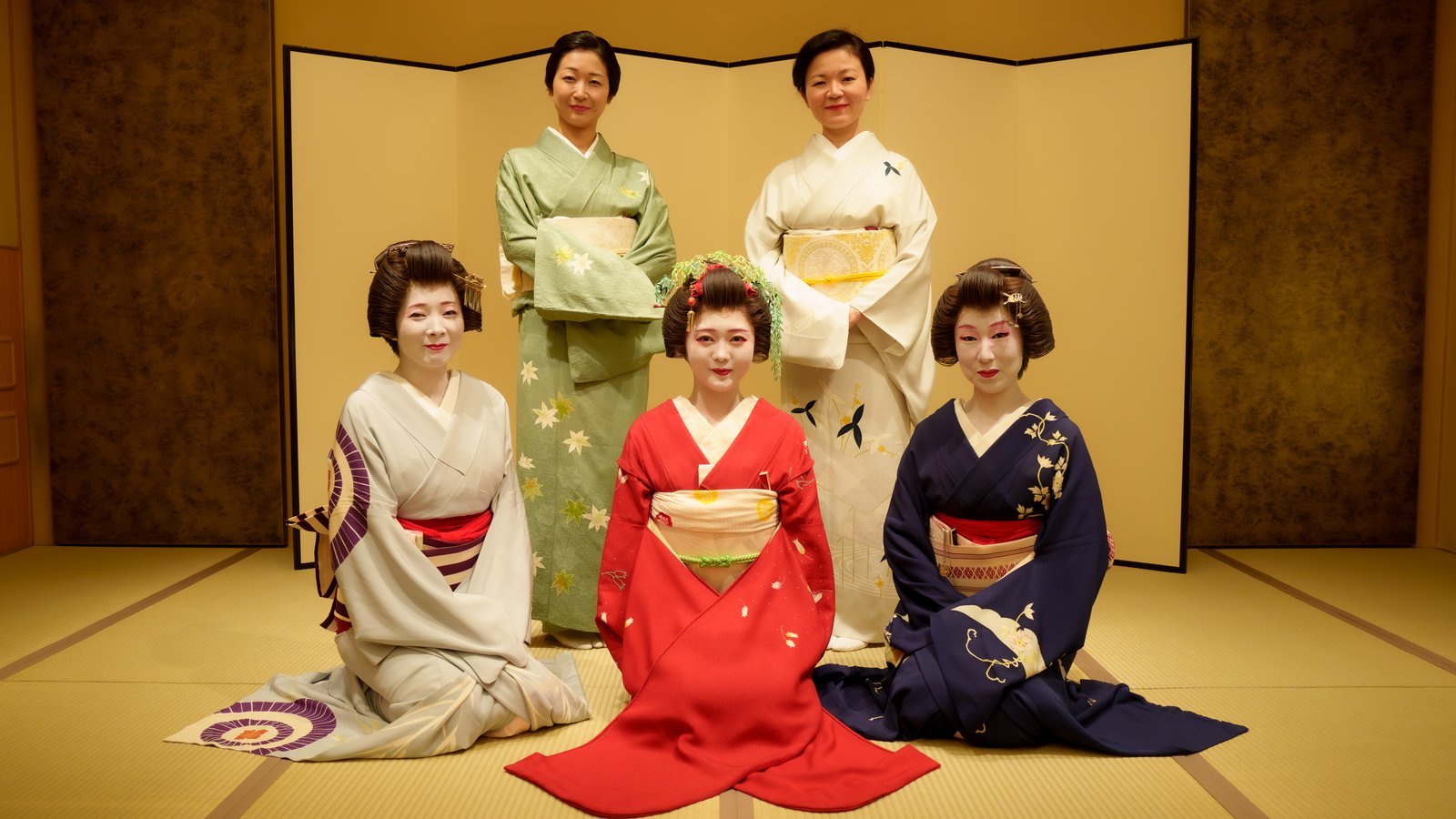 Asakusa geisha and the women who support them, gathered in formal kimono before a gold screen
