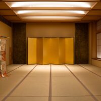 The main tatami room of an Asakusa house that hosts geisha evenings, with a gold folding screen set at the far end