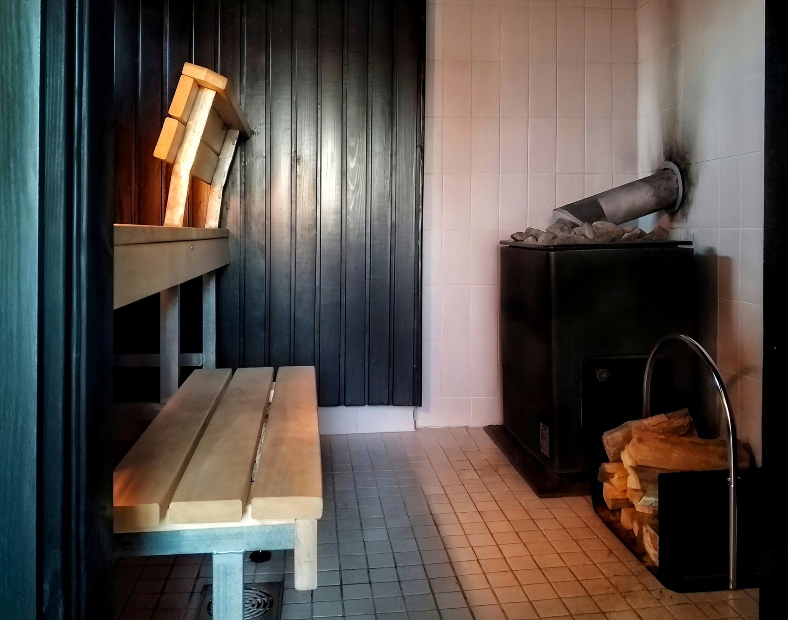 A sauna room with a wood-burning stove and stacked firewood