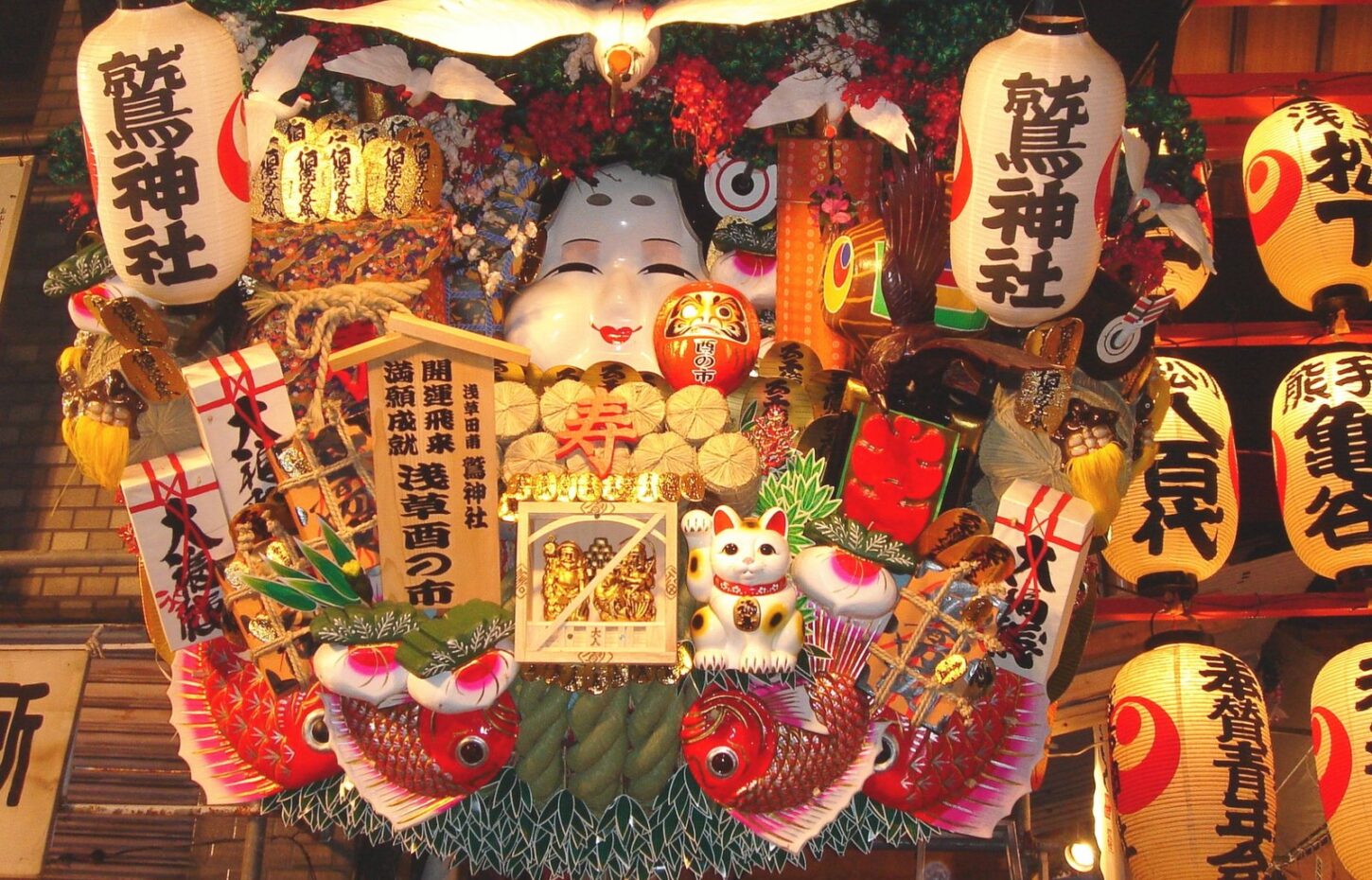 A large kumade rake with an Okame mask and sea bream, under - Asakusa Miyakodori A large kumade rake with an Okame mask and sea bream, under Otori Shrine lanterns at night
