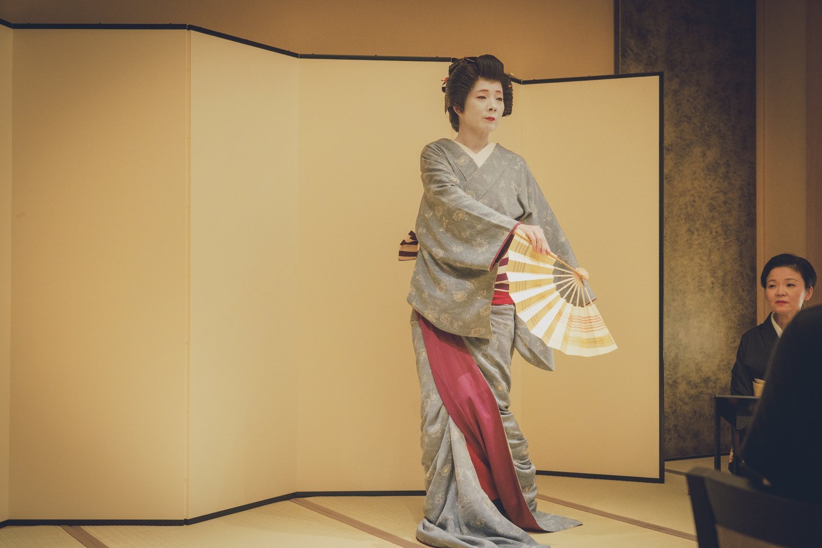An Asakusa geisha dancing with a fan before a gold screen at Miyakodori, with a jikata watching